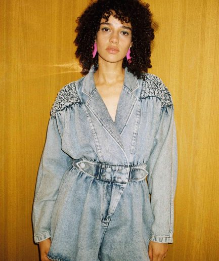Blue denim jumpsuit featuring gathered padded shoulder, wrap front style and self fabric covered button. Photo 1